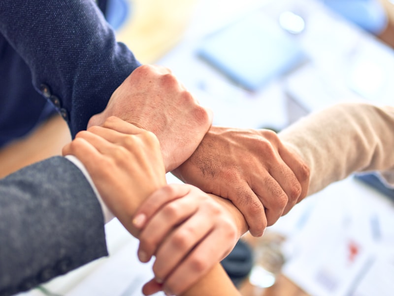 Several people clasping one another’s wrists in a circle above a desk