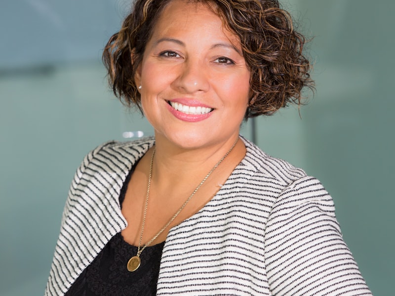 A person with curly hair smiling in a striped jacket, photographed indoors