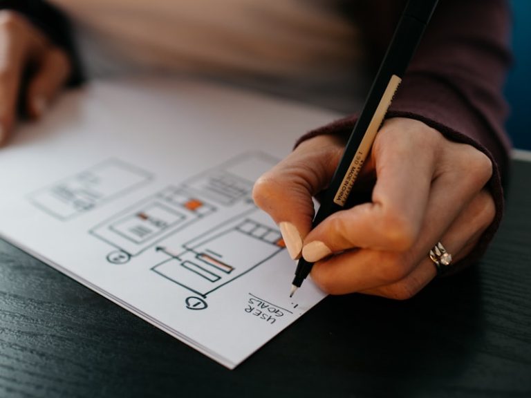 A hand sketching a mobile app wireframe layout on paper with a pencil
